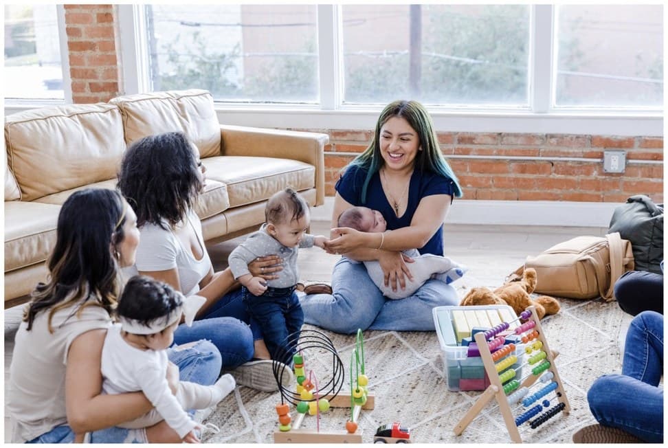 A small group of mothers sitting on the floor together with their babies and toys — laughing, sharing, and connecting in community
