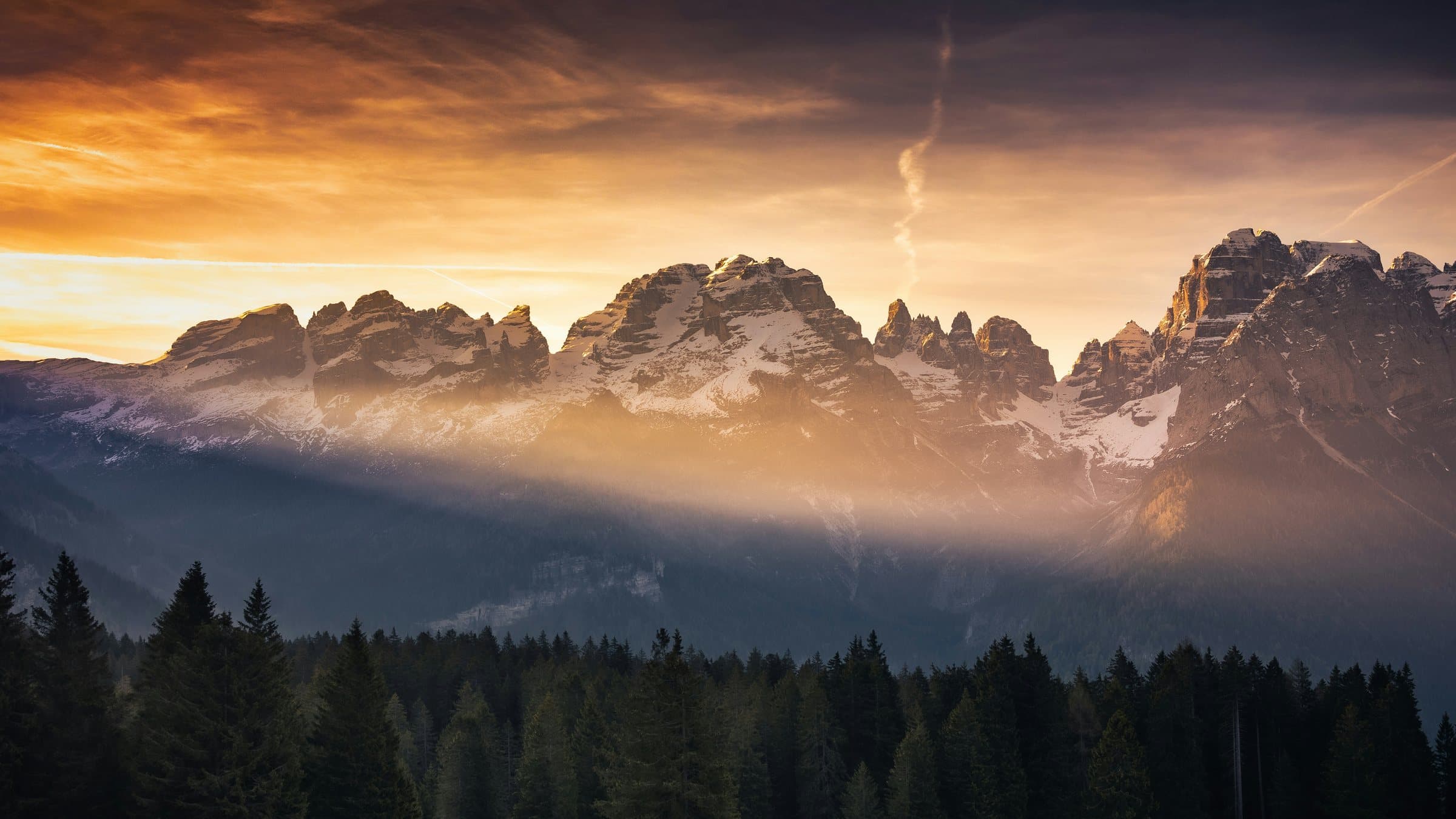 First light breaking over a mountain range above a dark pine forest